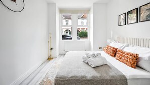 A modern bedroom with a large bed, a view of the street through a window, and a wall clock.