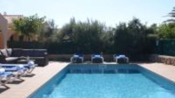 A rectangular swimming pool with lounge chairs and umbrellas along the side. - Villa Sa cova (Cap d'Artrutx)
