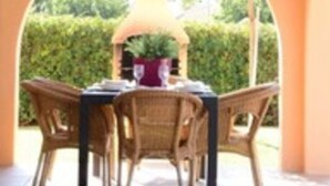 An outdoor dining area with wicker chairs and a table, under a pergola with a thatched roof. - Villa Sa cova (Cap d'Artrutx)