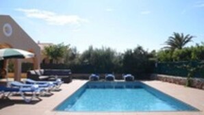 A swimming pool with lounge chairs and umbrellas, surrounded by greenery. - Villa Sa cova (Cap d'Artrutx)
