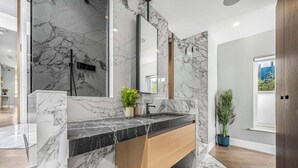 A modern bathroom with marble walls, a wooden vanity, a large mirror, and a potted plant. - Refined 2-Bed Soho Apartment with AC · Sleeps 6 (London)