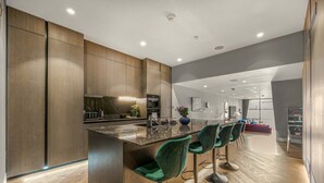 A modern kitchen with a central island, bar stools, and a dining area with a red sofa.