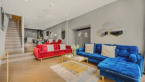 A modern living room with a red and blue sofa set, a coffee table, and a staircase leading to a dining area.
