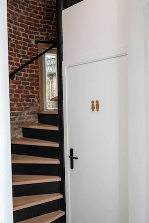 Un escalier aux marches noires mène à une porte blanche dotée d’une poignée noire. On peut voir deux figurines en bois sur la porte.