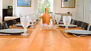 A dining room with a long table set for a meal, surrounded by chairs, with a vase centerpiece and framed artwork on the walls.