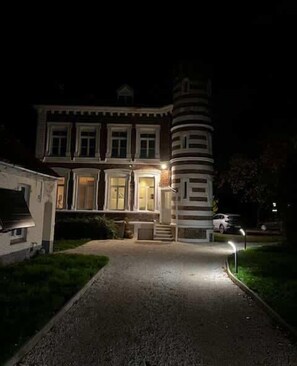 A large, historic building with a prominent tower and a well-lit entrance. - La Magnifique - Prestige - Parc - Art et Histoire (Aire-sur-la-Lys)