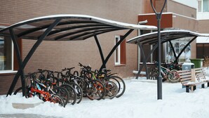 Un área de estacionamiento cubierto para bicicletas, con bicicletas y un banco en la nieve.