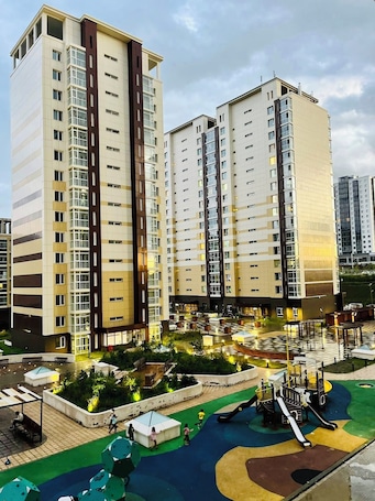 A high-rise residential building with multiple balconies, a rooftop garden, and a playground area.