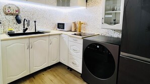 Una cocina compacta con armarios blancos, lavadora negra, microondas y un lavabo.