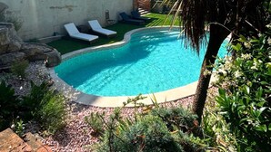 Una piscina con sillones de descanso, rodeada de rocas y plantas.