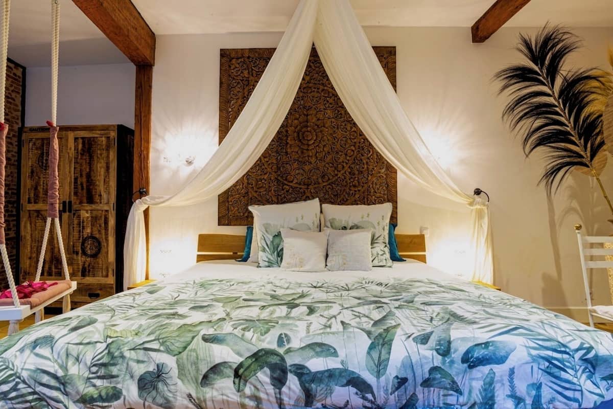 A bed with a canopy, a wooden headboard, and a tropical-themed bedspread.