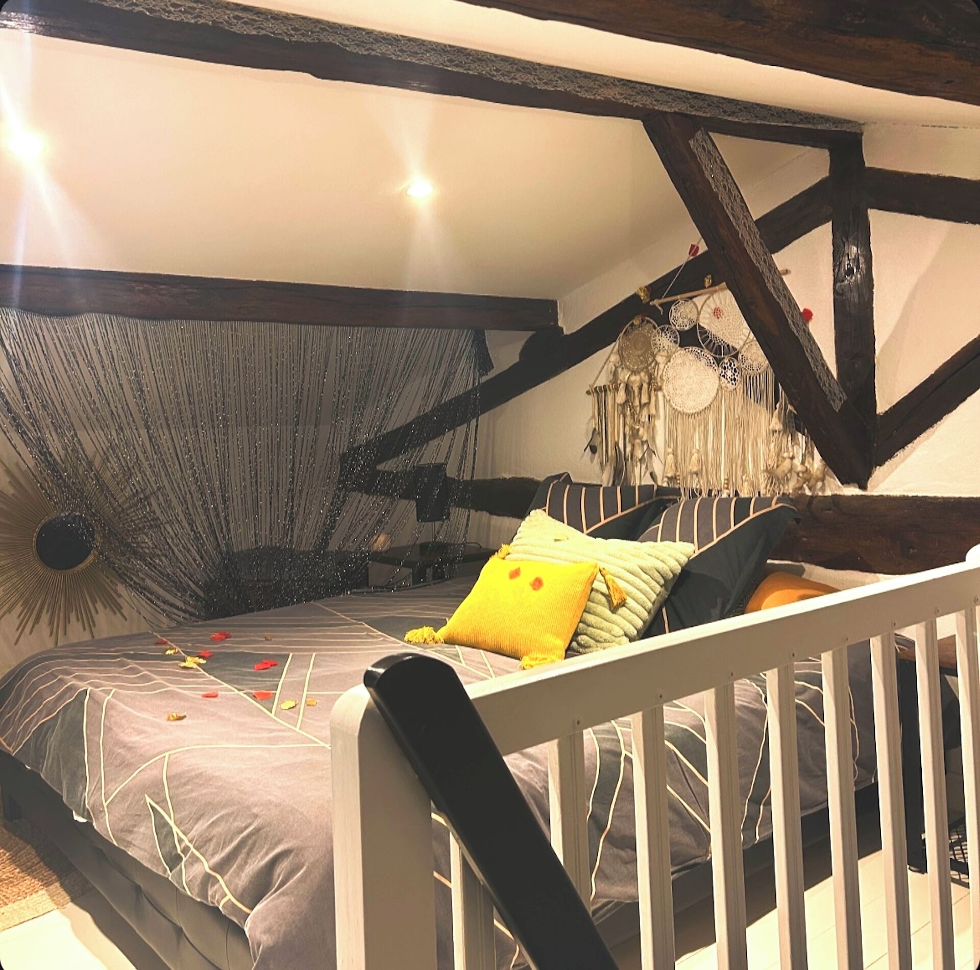 Une chambre avec un plafond en pente, des poutres apparentes, un lit avec une literie à motifs et un attrape-rêves en guise de décoration.