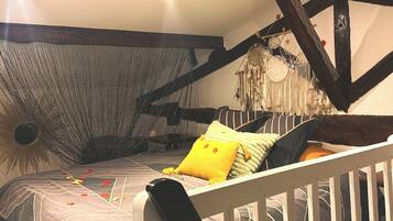 Une chambre avec un plafond en pente, des poutres apparentes, un lit avec une literie à motifs et un attrape-rêves en guise de décoration.