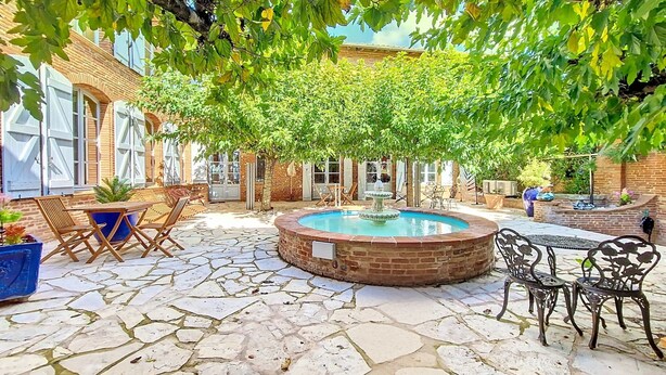 Un patio con piscina, mobiliario exterior y un edificio de ladrillo.
