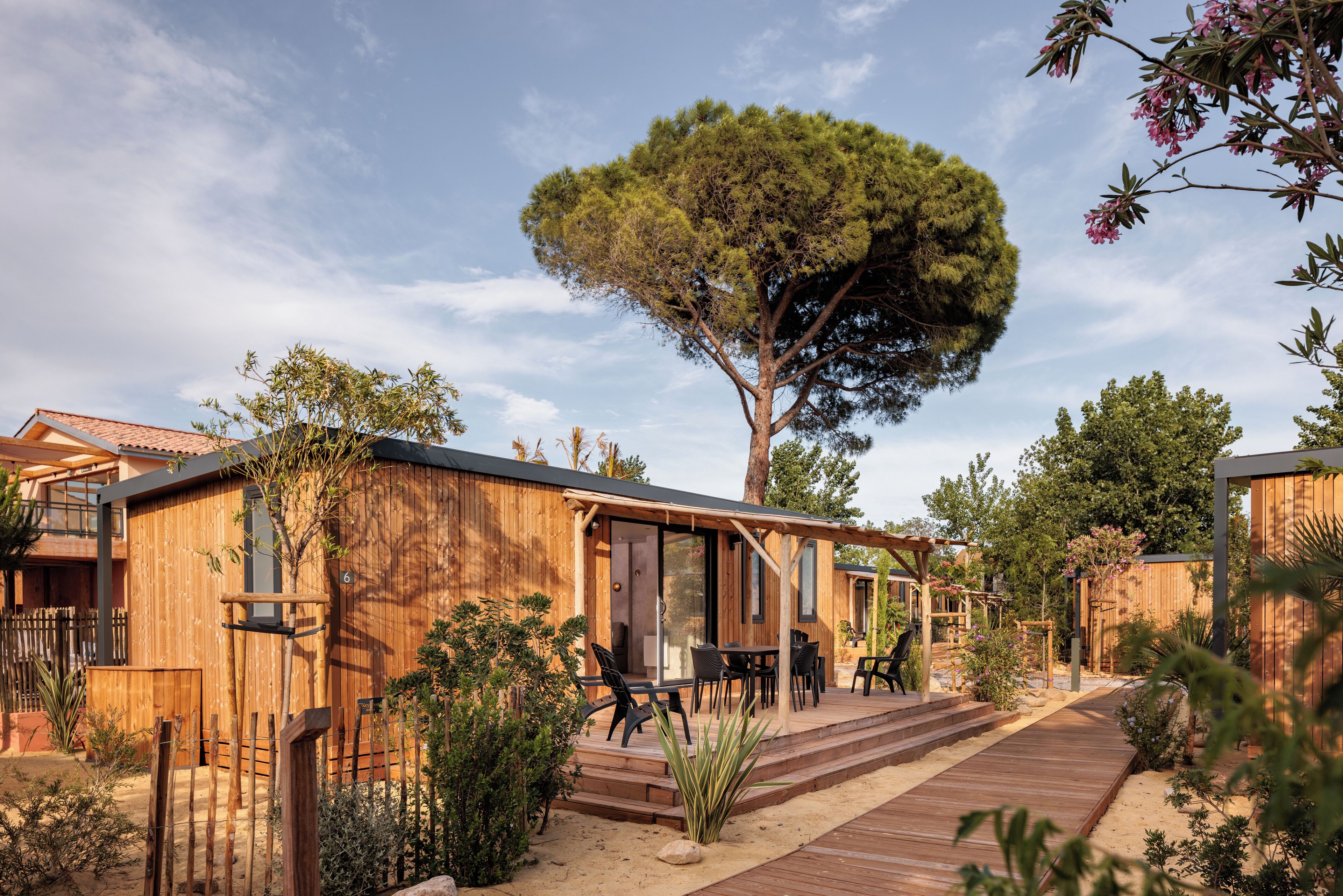 Eine Holzhütte mit einer Terrasse, umgeben von Vegetation und einem großen Baum.