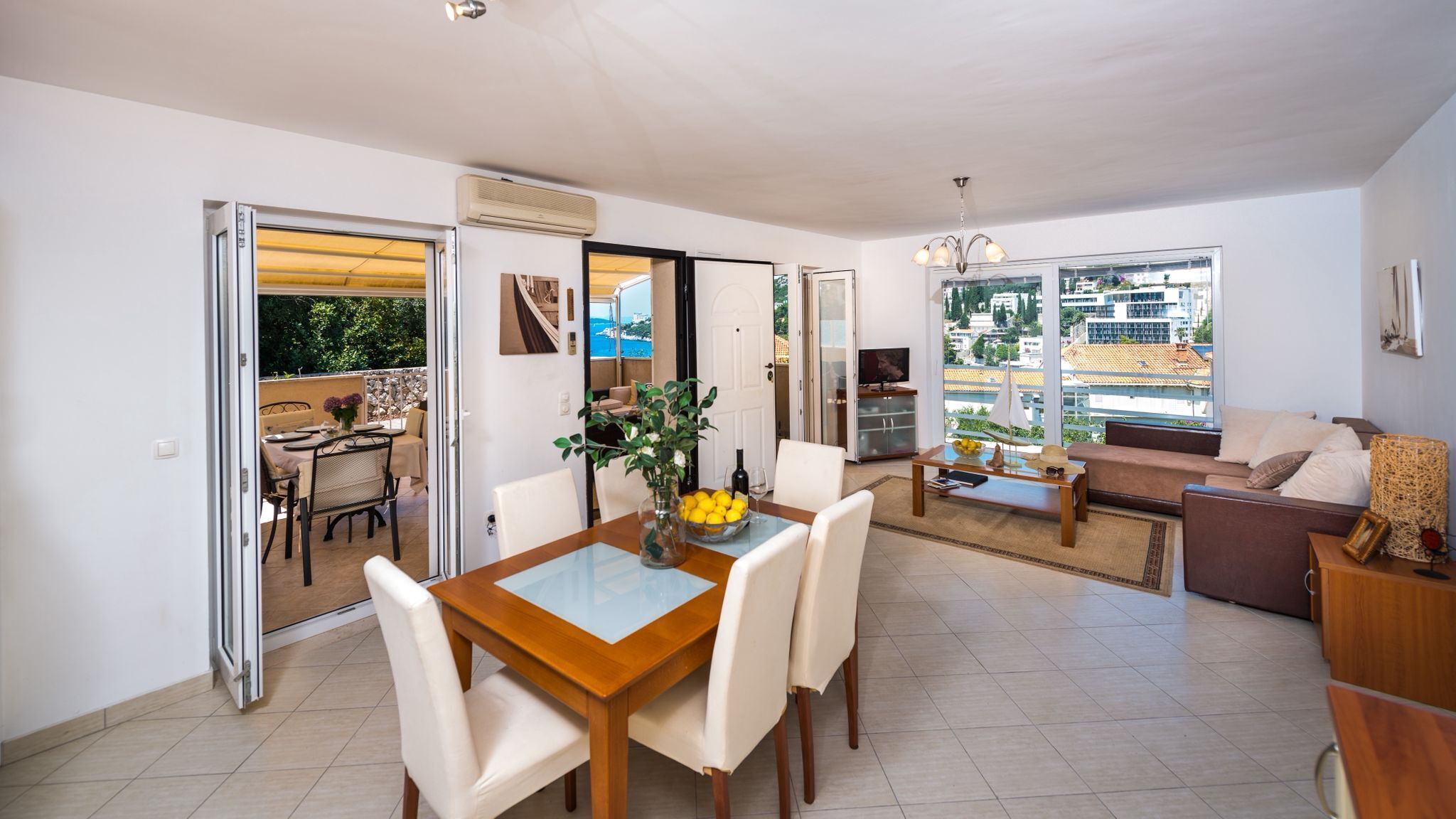 A modern apartment with a dining area, a living room with a sofa, and a balcony with a table and chairs.