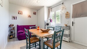 Una habitación acogedora con una mesa de madera, sillas, un sofá púrpura y una ventana con cortinas.