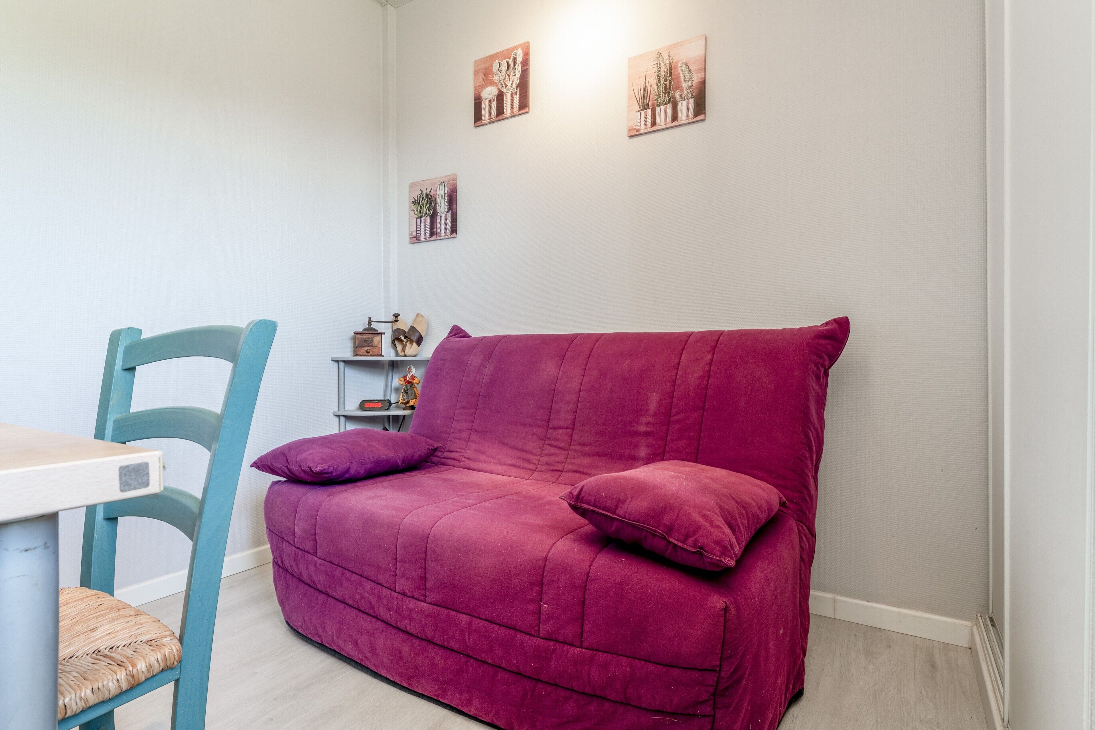 Una habitación con una silla verde azulada, un sofá púrpura y una mesita de noche con una lámpara.