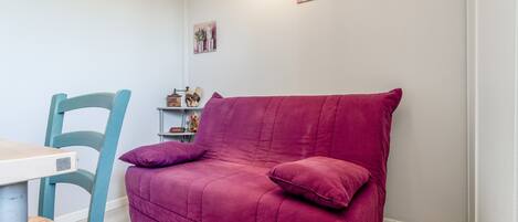 Una habitación con una silla verde azulada, un sofá púrpura y una mesita de noche con una lámpara.