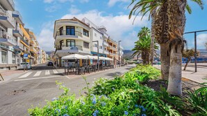 Una calle con un café, mesas al aire libre y una palmera.