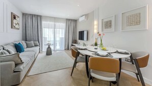 Una sala de estar moderna con un sofá gris, una mesa de comedor con platos, vasos y una botella, y un televisor montado en la pared.