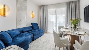 En moderne stue med en blå sofa, en væg med marmorudsmykning og et spiseområde med et rundt bord dækket til seks personer.