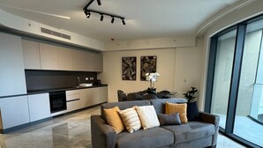 A modern living room with a grey sofa, a dining area, and a kitchen.