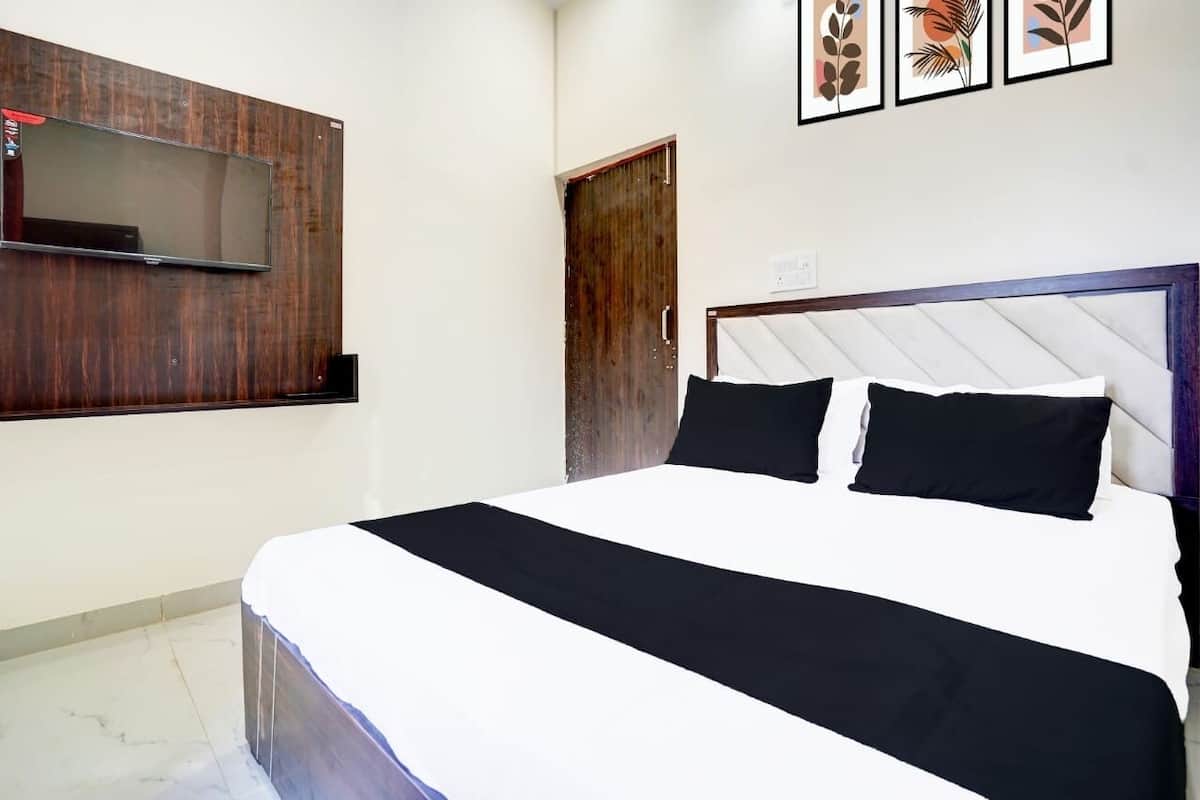 A bedroom with a bed, a television mounted on the wall, a wooden door, and framed artwork on the wall.