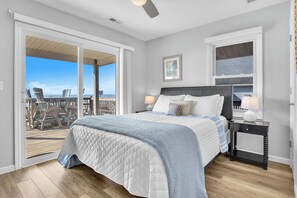 A bedroom with a bed, a nightstand, a window, and a view of the beach.