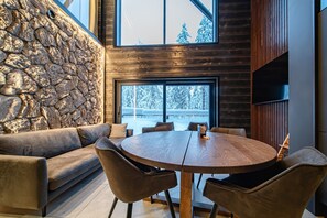 Un interior moderno con una pared de piedra, una mesa de comedor de madera con sillas y vistas a un paisaje nevado a través de amplios ventanales.