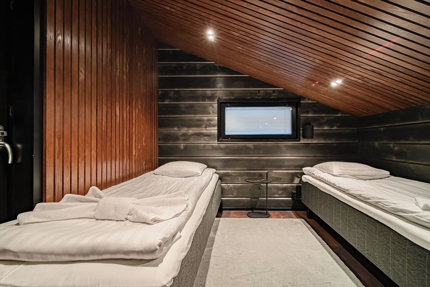 A compact bedroom with two single beds, a small table, and a TV mounted on the wall.