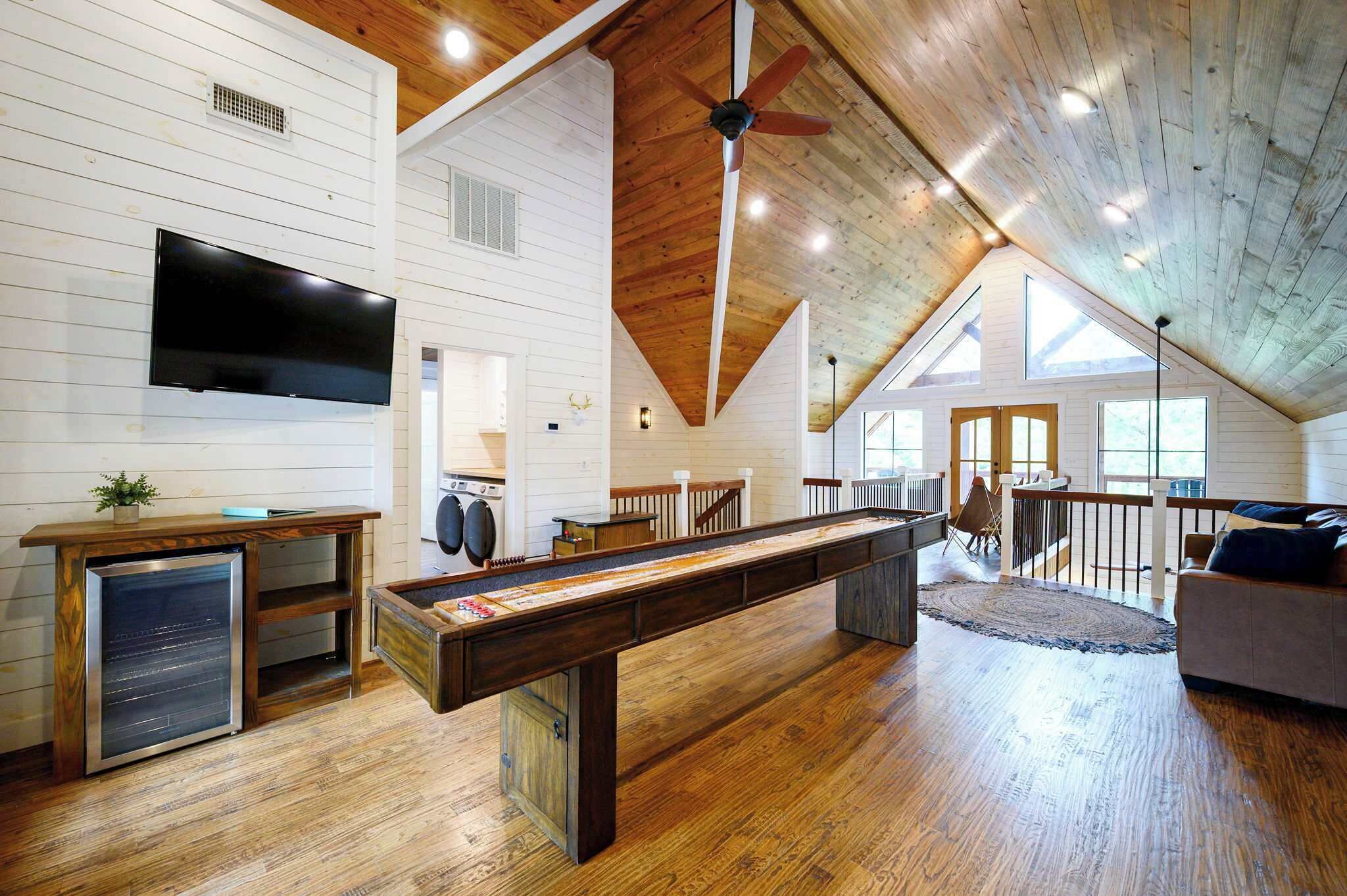 A spacious loft-style room with a pool table, a flat-screen TV, and a wooden ceiling.
