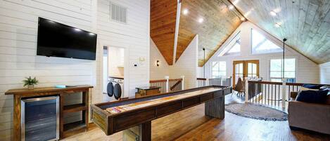 A spacious loft-style room with a pool table, a flat-screen TV, and a wooden ceiling.