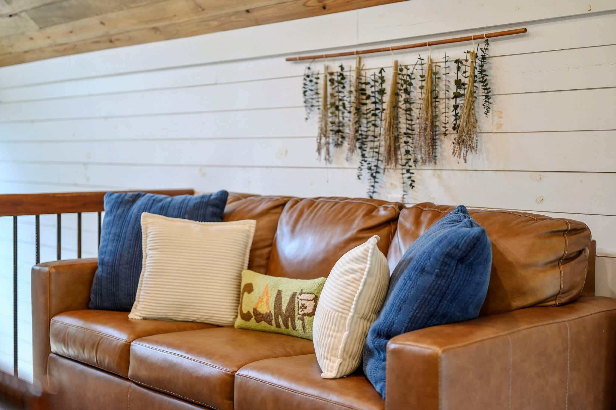Een bruine leren bank met meerdere kussens, een houten plafond en een wandplank met planten.