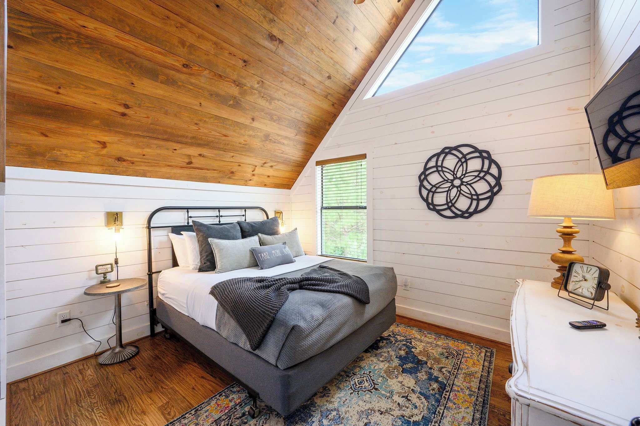 Une chambre avec un plafond en pente, un lit avec des oreillers, une table de chevet avec une lampe et une horloge murale.