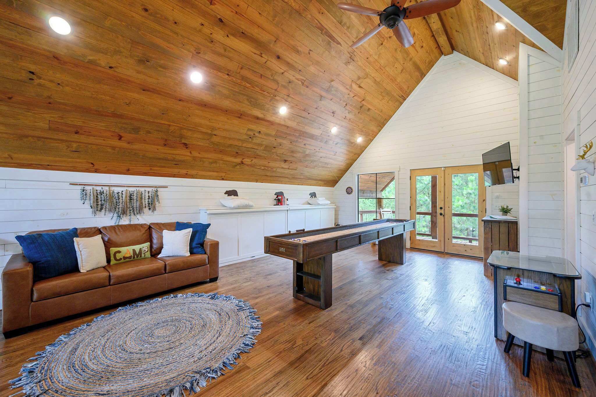 A spacious loft with a wooden ceiling, a pool table, a brown leather sofa, and a dining area with a small table and chairs.