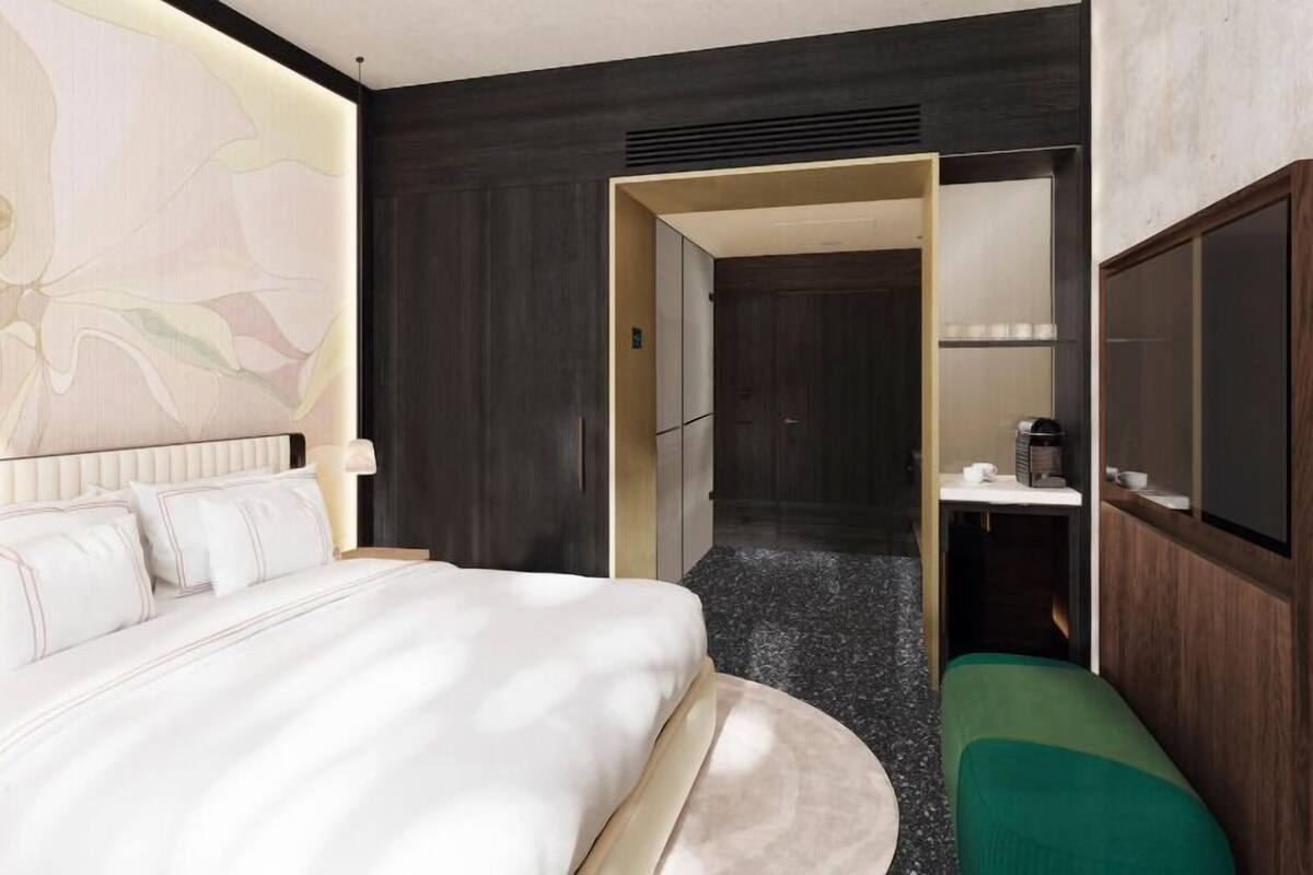 A hotel room with a bed, a green bench, a small table with a cup, and a large abstract painting on the wall.
