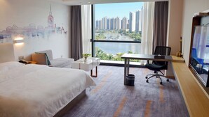 Habitación de hotel con una cama grande, un escritorio, una silla, un televisor y vistas a un paisaje urbano y al río.