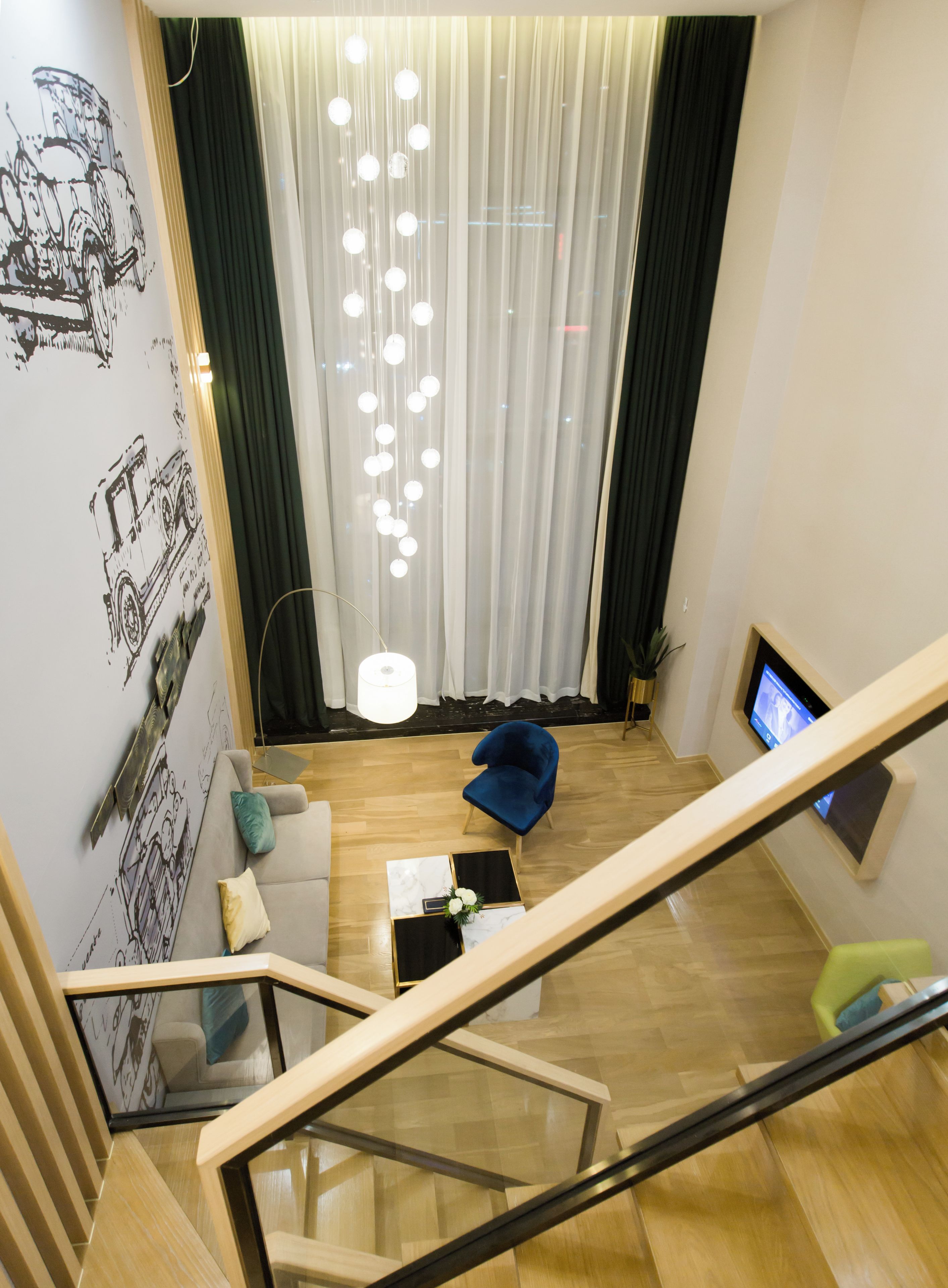 A modern loft suite with a staircase, a sofa, a blue chair, and a TV on the wall.