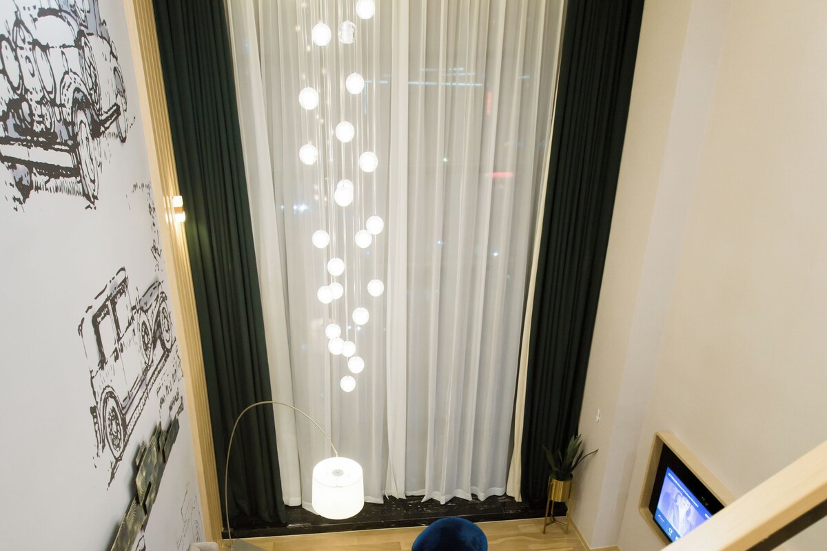 Une suite moderne de style « loft », dotée d’un escalier, d’un canapé, d’un fauteuil bleu et d’un téléviseur fixé au mur.