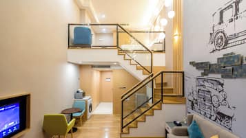 Una suite tipo loft con escalera, un sofá, una mesa de centro, un televisor y una lavadora.