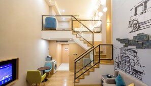 Une suite de style loft comprenant un escalier, un canapé, une table basse, un téléviseur et un lave-linge.