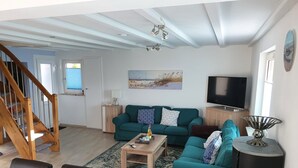 A living room with a green sofa, wooden coffee table, and a TV. There's a staircase and a door leading outside. - Haus 53° Nord - North Sea vacation for the whole family - pets welcome (Südbrookmerland)