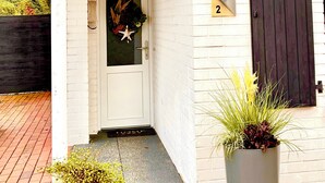 A white building with a black door, a number '2' sign, and a potted plant on the porch. - Haus 53° Nord - North Sea vacation for the whole family - pets welcome (Südbrookmerland)