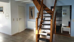 A spacious living area with a wooden staircase leading to an upper floor. - Haus 53° Nord - North Sea vacation for the whole family - pets welcome (Südbrookmerland)