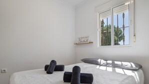 A bedroom with a bed, pillows, a window, and a shelf with a picture.