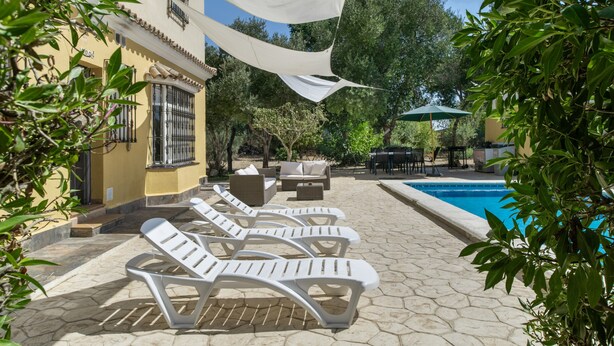 A pool area with lounge chairs, a table, and a covered seating area.