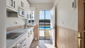 A kitchen with white cabinets, a microwave, and a view of a swimming pool through an open door.