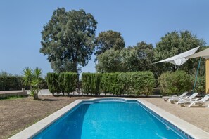 Ein Schwimmbecken mit Liegestühlen, umgeben von ordentlich geschnittenen Hecken und Bäumen.