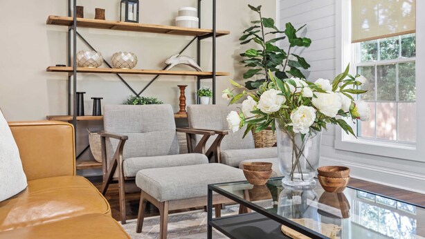A living room with a glass coffee table, two grey armchairs, a brown sofa, a wooden bookshelf, and a vase of white flowers. - Call Me Old Fashioned! *Heart of Bardstown Square* (Bardstown)